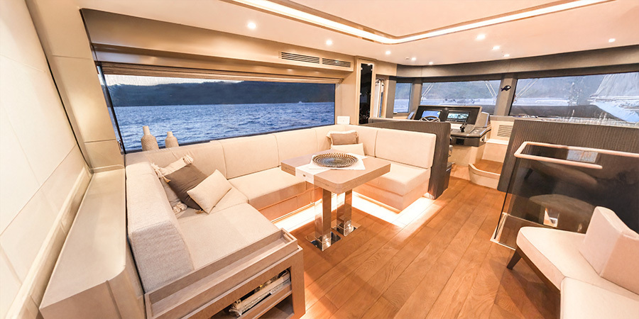 Spacious yacht interior with panoramic windows and ambient lighting, including subtle toe kick lights under the furniture.