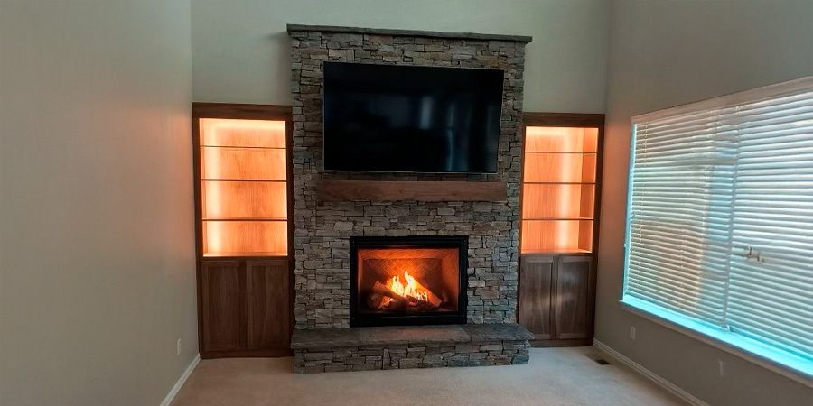  A living room featuring a stone fireplace as the focal point, with built-in shelves on either side illuminated by warm lights, creating a welcoming atmosphere.