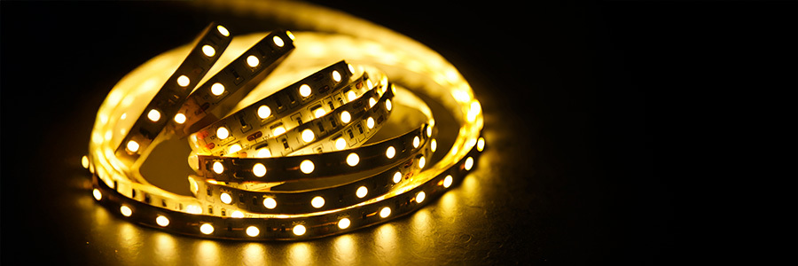 Orange-lit house outline enhancing the Halloween atmosphere.A roll of warm yellow LED strip lighting coiled on a dark surface. The lights are turned on, illuminating the strip and creating a warm glow.