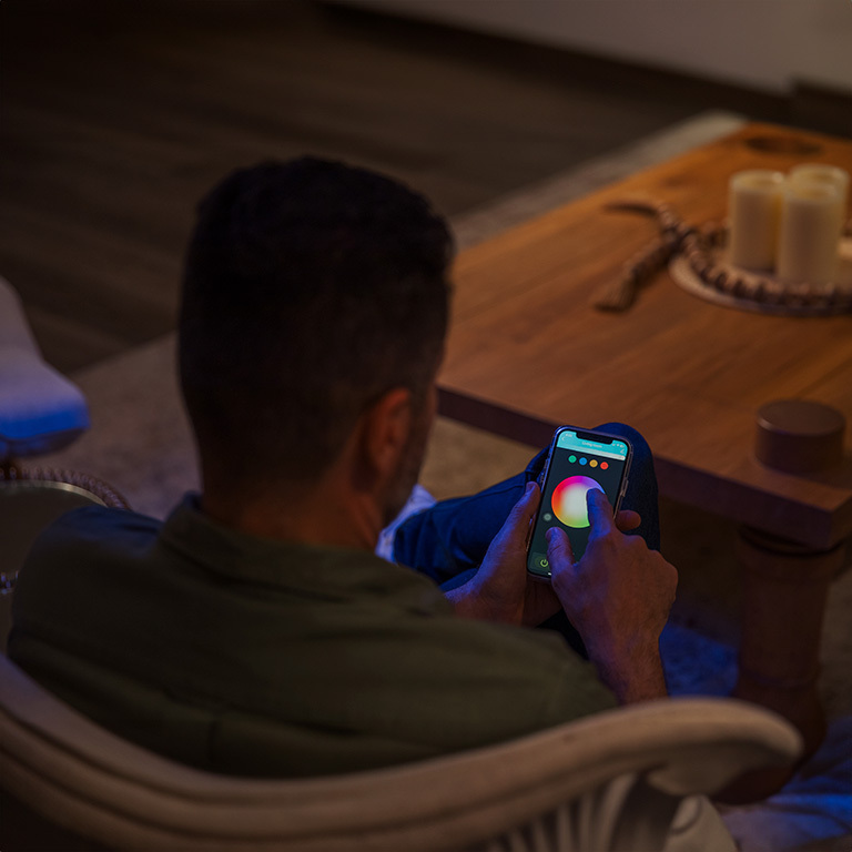 man-holding-phone-with-digital-rgb-controller A man holding a smartphone displaying a digital RGB controller app on the screen, with various color options and adjustment settings visible for controlling LED strip lights.