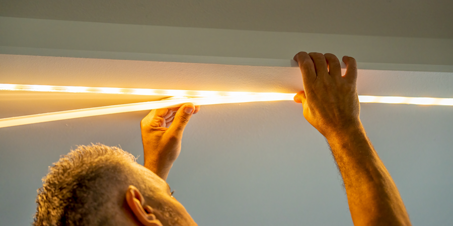 Man installing LED strip lights on a ceiling, securing a diffuser cover to evenly distribute the warm light.