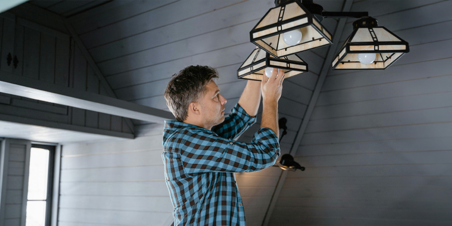 Man in a plaid shirt putting a LED light bulb in new lamps.