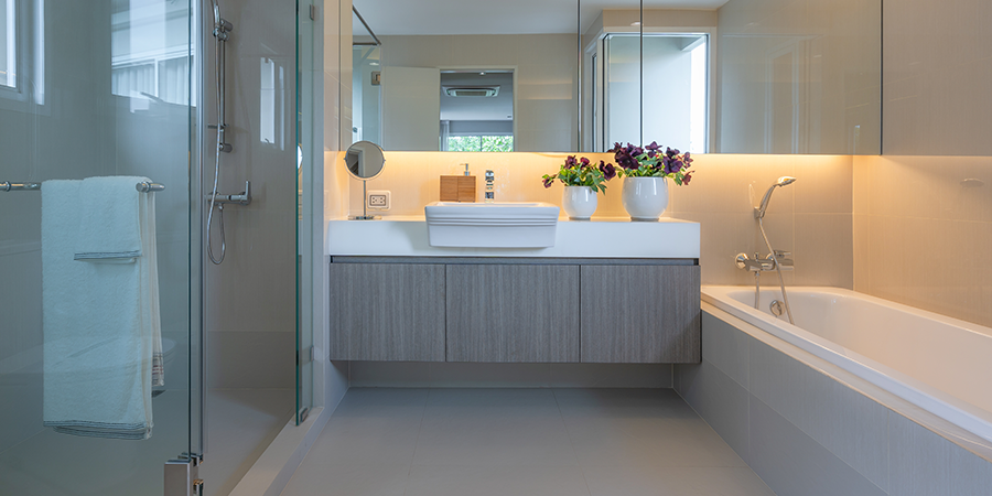 A contemporary bathroom featuring a glass-enclosed shower, floating vanity with integrated LED lighting, a large mirror, a bathtub, and decorative flower arrangements for a stylish and functional design.