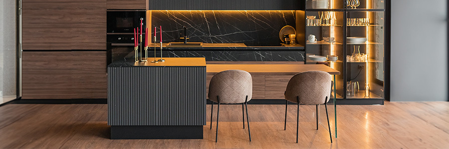 A modern kitchen featuring wooden cabinets, black marble countertops, LED strip lighting under the cabinetry, and illuminated glass shelves with elegant dinnerware and glasses.