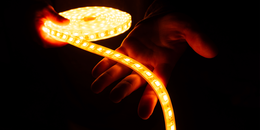  Person holding a glowing LED strip light emitting warm orange light in a dark setting.