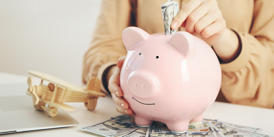 Saving Money with a Piggy Bank Pink piggy bank with cash and a wooden airplane on a white table