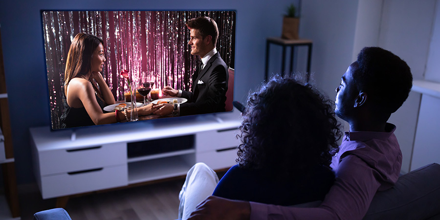 Couple having a cozy Valentine's Day movie night at home with TV backlighting