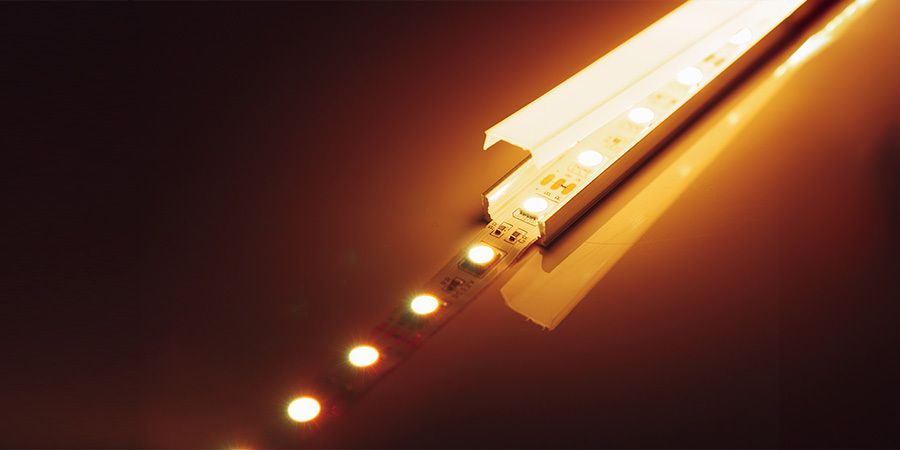 A warm LED strip light installed in an aluminum channel, emitting a soft, warm glow with reflections on a smooth surface, showcasing its structured design and illumination.